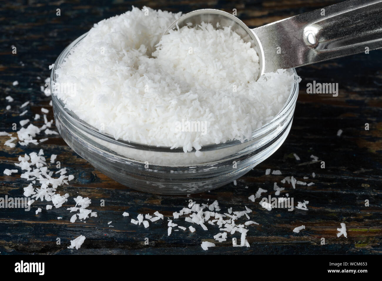 Shredded Coconut In Spoon By Bowl On Wooden Table Stock Photo