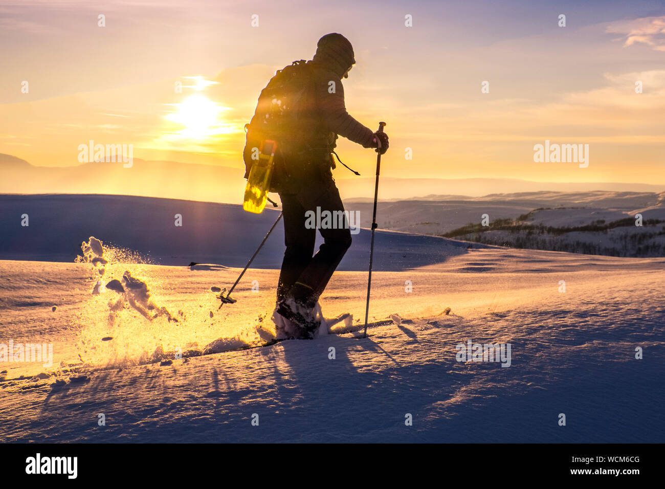 Ski tourer / cross country skier / back country skier silhouetted against the setting sun in the mountains of Norway Stock Photo