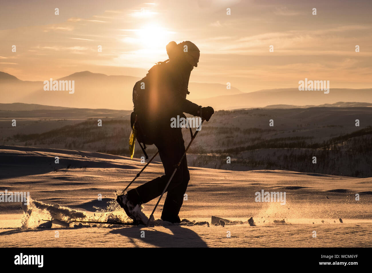 Ski tourer / cross country skier / back country skier silhouetted against the setting sun in the mountains of Norway Stock Photo