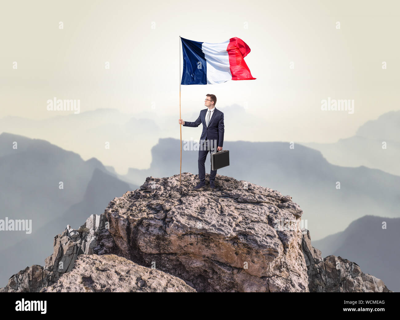 Successful businessman on the top of a mountain holding France victory ...