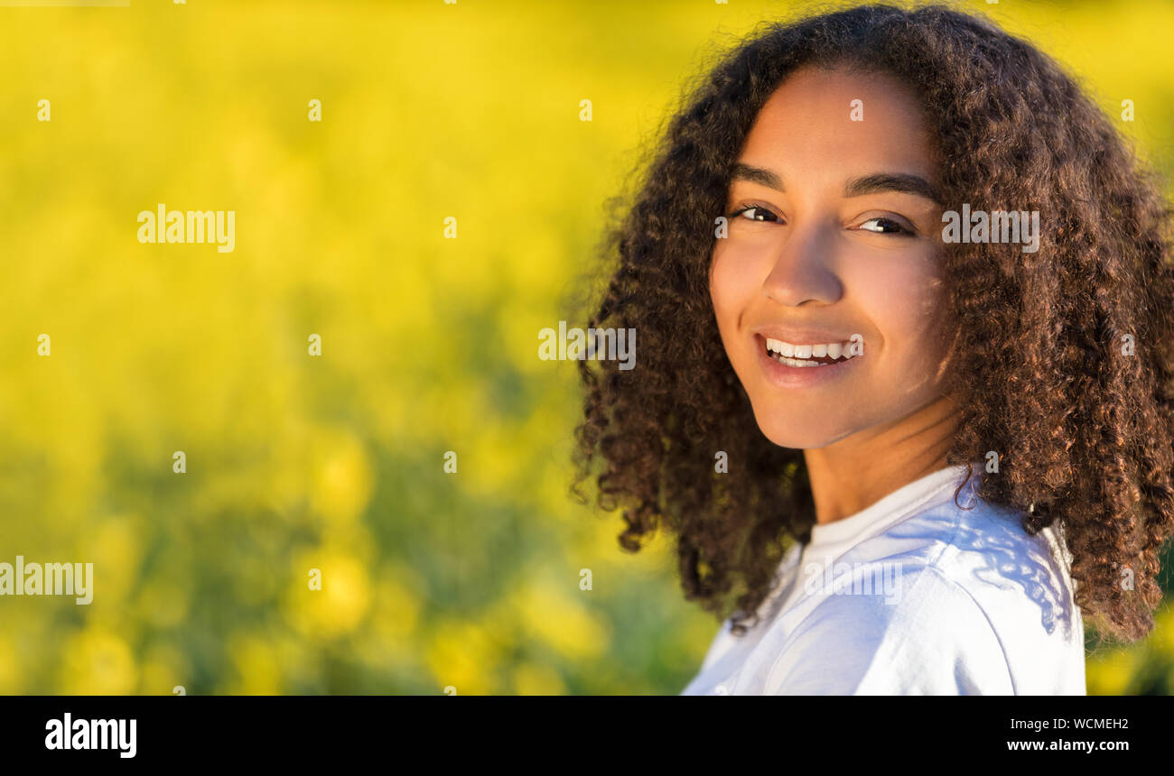 Beautiful mixed race biracial African American girl teenager female young woman smiling and happy in a field of yellow flowers Stock Photo
