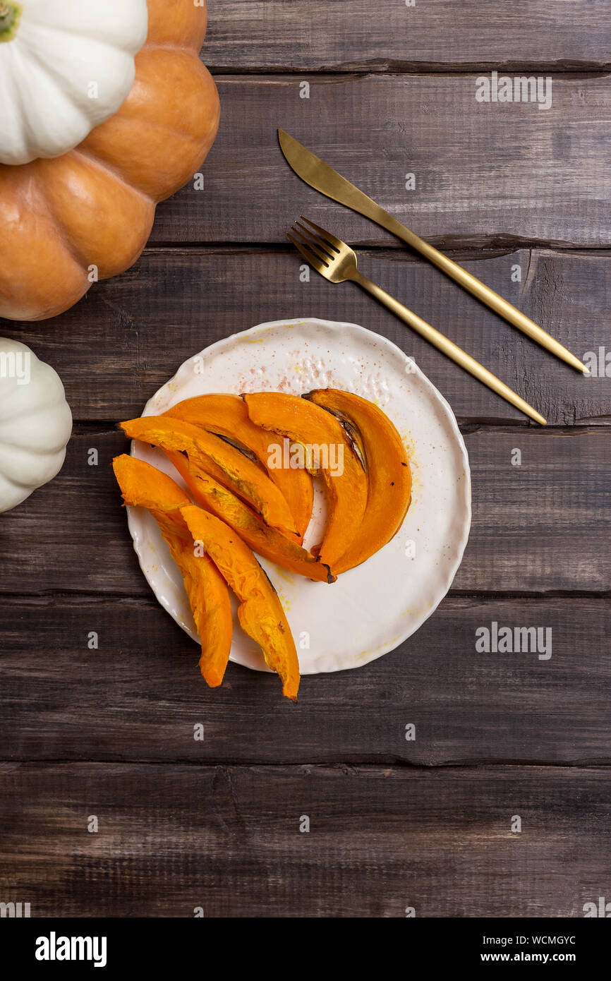 Baked pumpkin on plate with tableware on wood background with seasonal decor. Concept of autumnal dinner. Top view, flat lay. October's food Stock Photo
