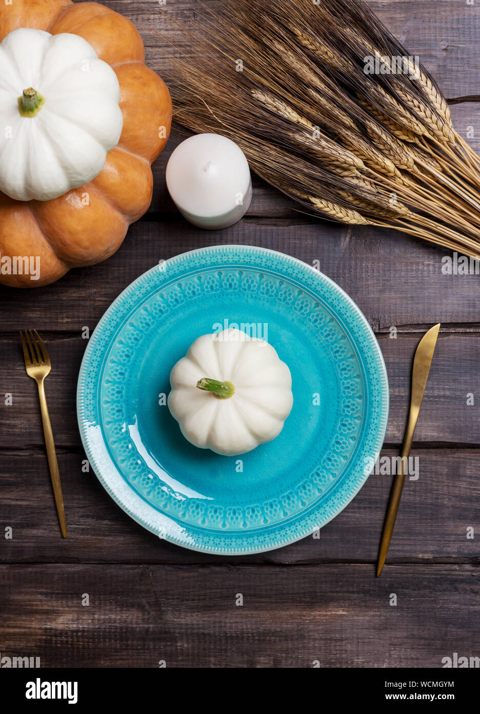 Blue serving plate with white baby squash on it, golden tableware, candle and wheat on wooden table. Concept of harvest table set, dinning for Thanksg Stock Photo