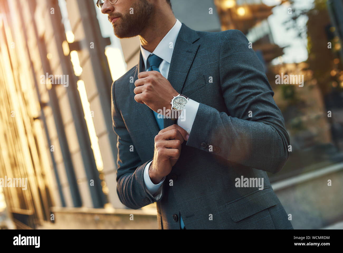 Stylish man. Confident businessman in full suit adjusting his sleeve while standing outdoors. Business concept. Stylish people Stock Photo