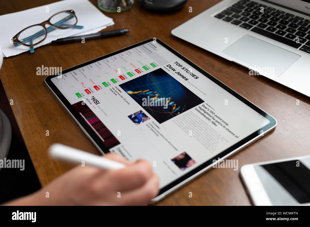 BATH, UK - AUGUST 28, 2019 : Person using an Apple iPad Pro on a desk displaying stock market information using the Apple Stock app. The page displays Stock Photo