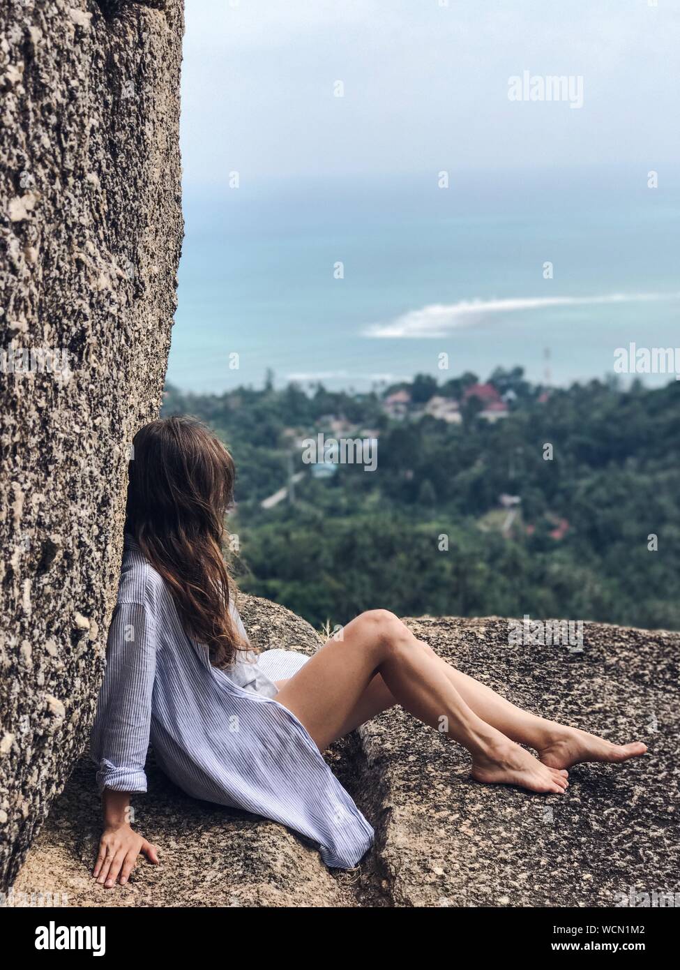 Side View Of Woman Sitting On Cliff Against Sea At Ko Samui Stock Photo