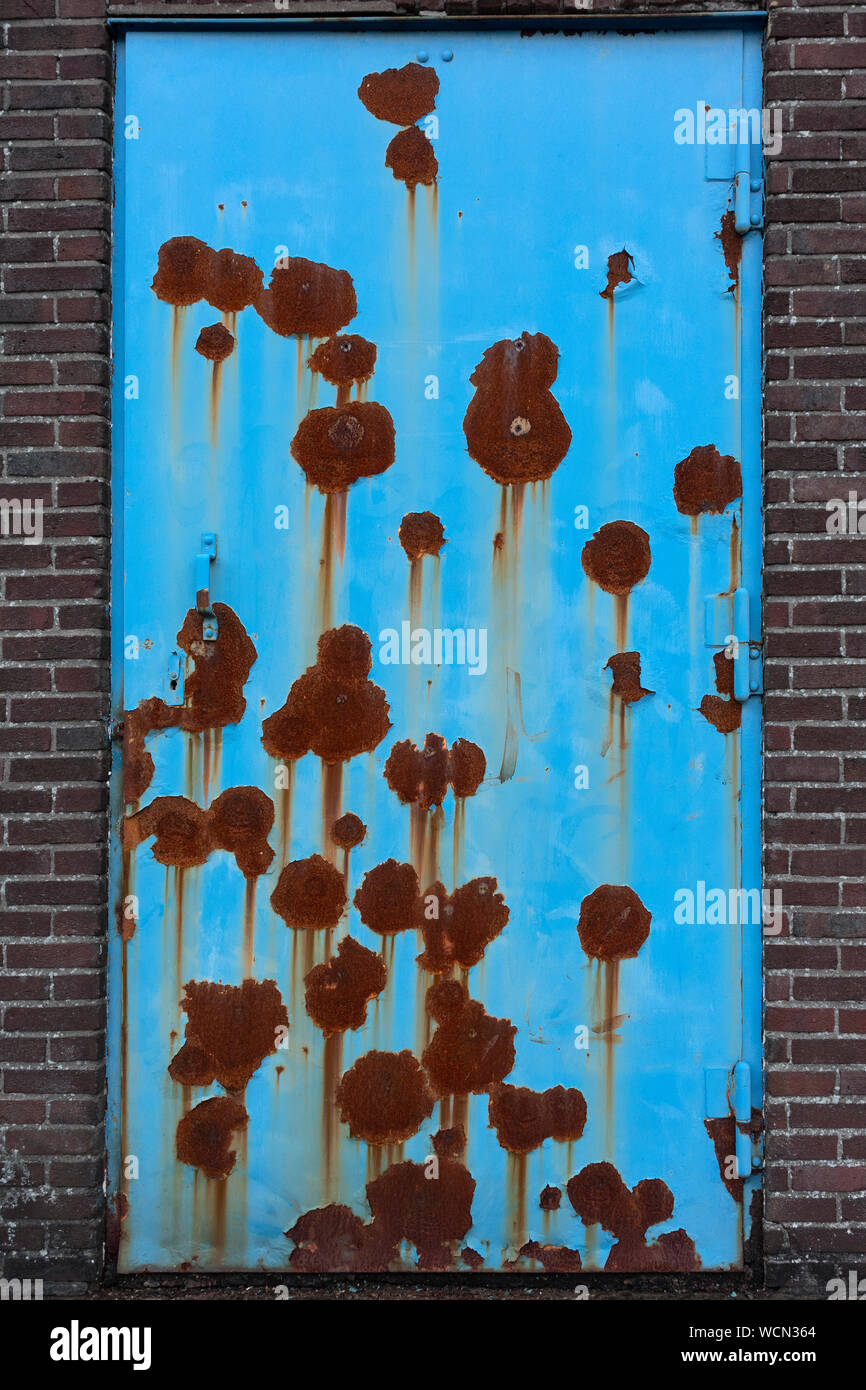 Closed blue neglected rusty door in a stone wall Stock Photo