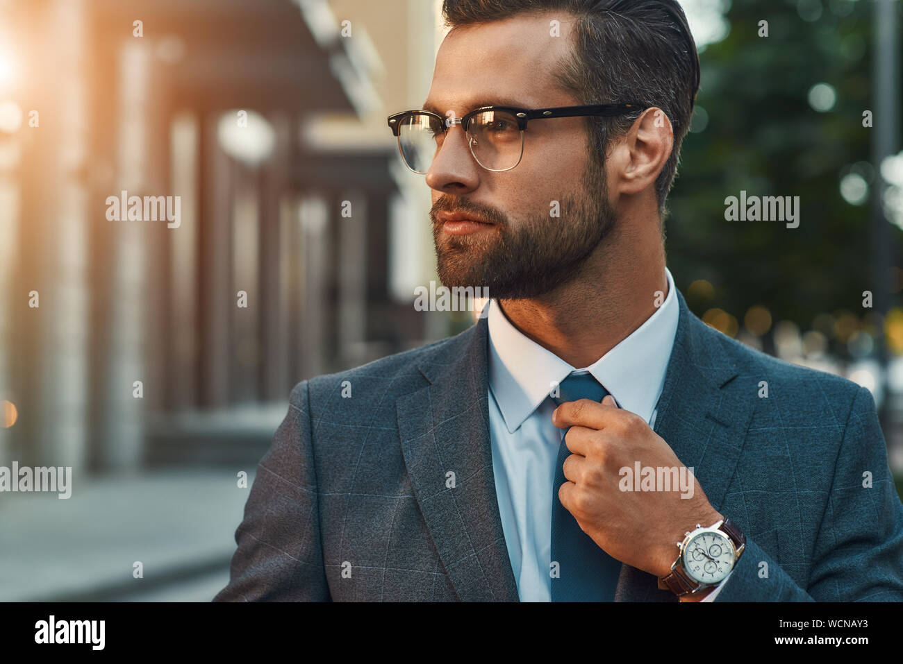 Great look. Confident businessman in full suit adjusting his tie and looking away while standing outdoors. Business concept. Stylish people Stock Photo