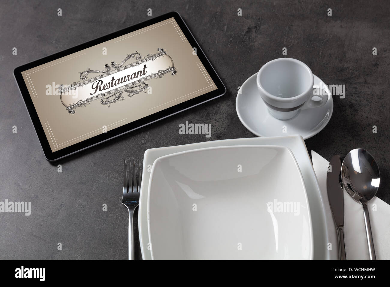 Tablet with stylish restaurant logo and laid table Stock Photo