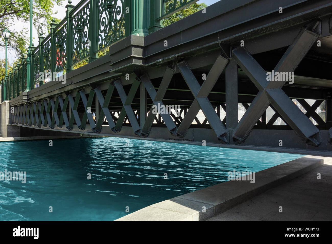Bridge across water channel. Metal frame structure over pure calm river. Modern urban city landscape with perspective view from stone bank or riversid Stock Photo