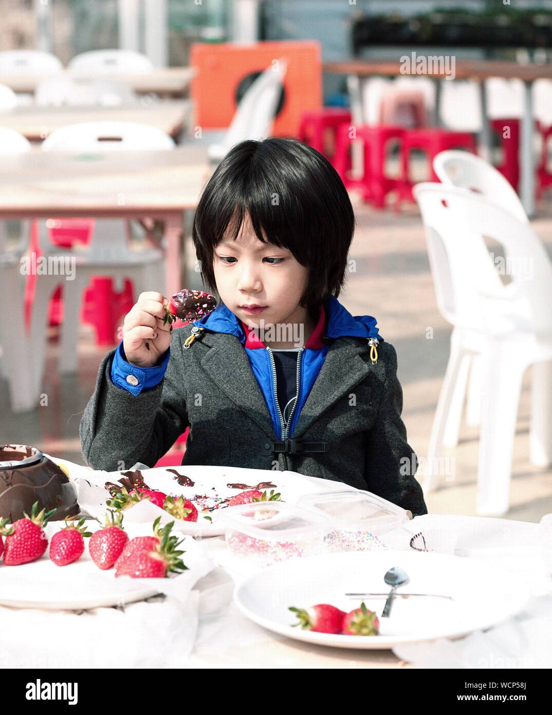Young Child Holding Chocolate Covered Strawberry At Table Stock Photo