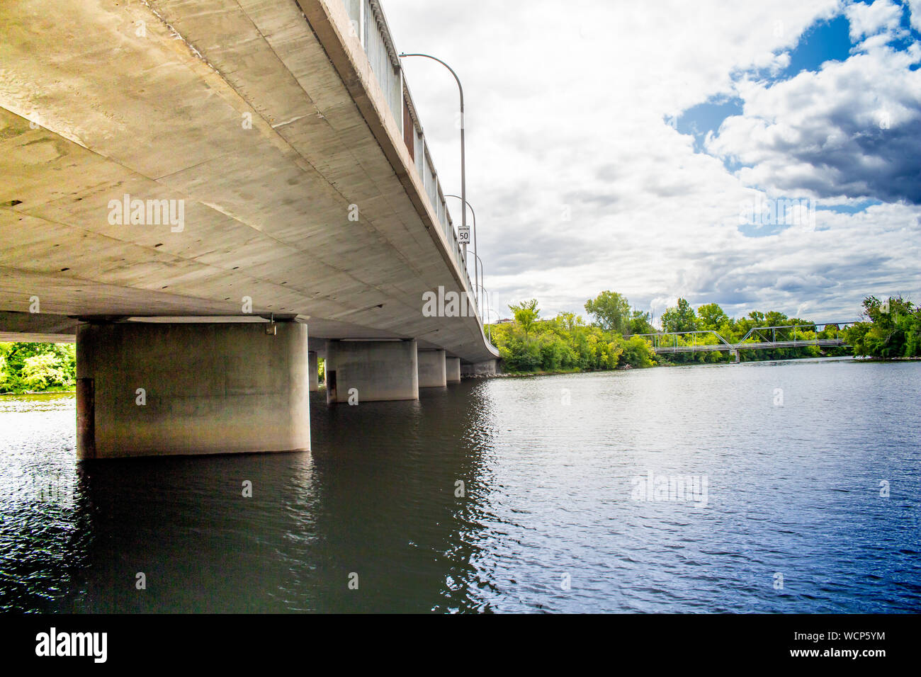Rippling water of a river flows under a concrete roadway bridge, viewed from below. Stock Photo
