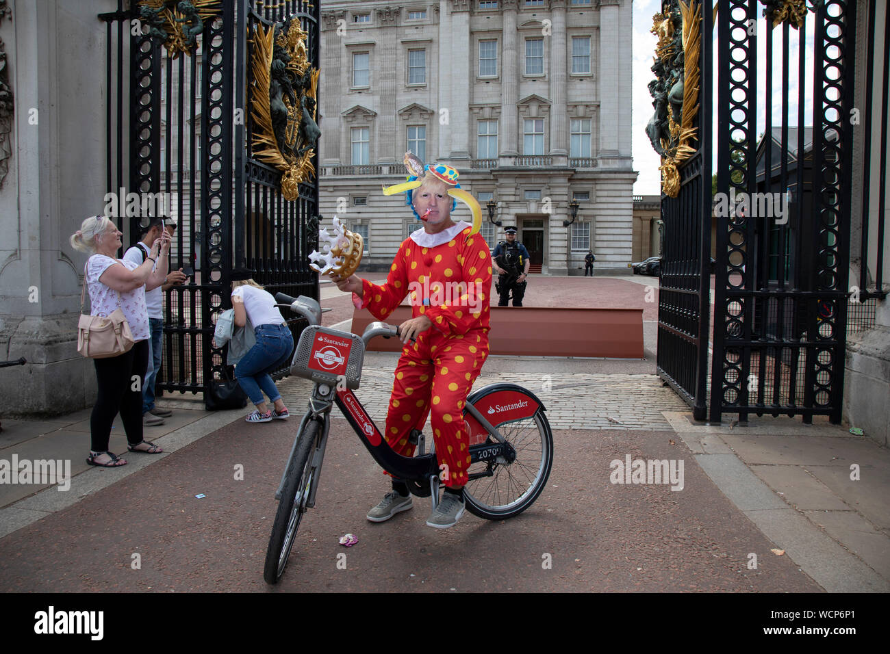 Anti Brexit protester dressed up as a clown version of Prime Minister Boris Johnson hires a Boris bike in Westminster and cycles to the gates of Buckingham Palace as it is announced that Boris Johnson has had his request to suspend Parliament approved by the Queen on 28th August 2019 in London, England, United Kingdom. The announcement of a suspension of Parliament for approximately five weeks ahead of Brexit has enraged Remain supporters who suggest this is a sinister plan to stop the debate concerning a potential No Deal. Stock Photo