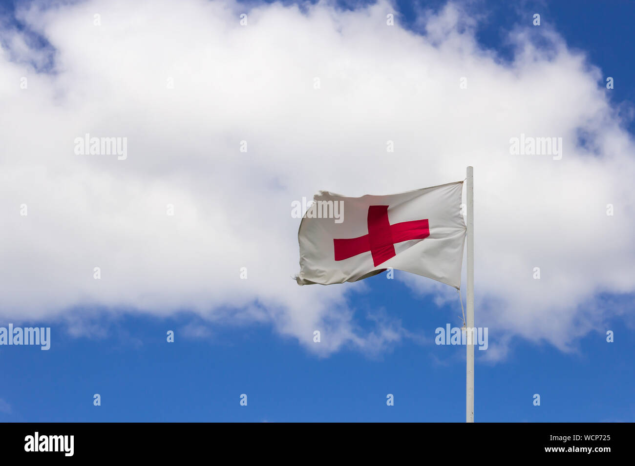 Flag of the Red Cross in the wind against a blue sky with clouds. Stock Photo