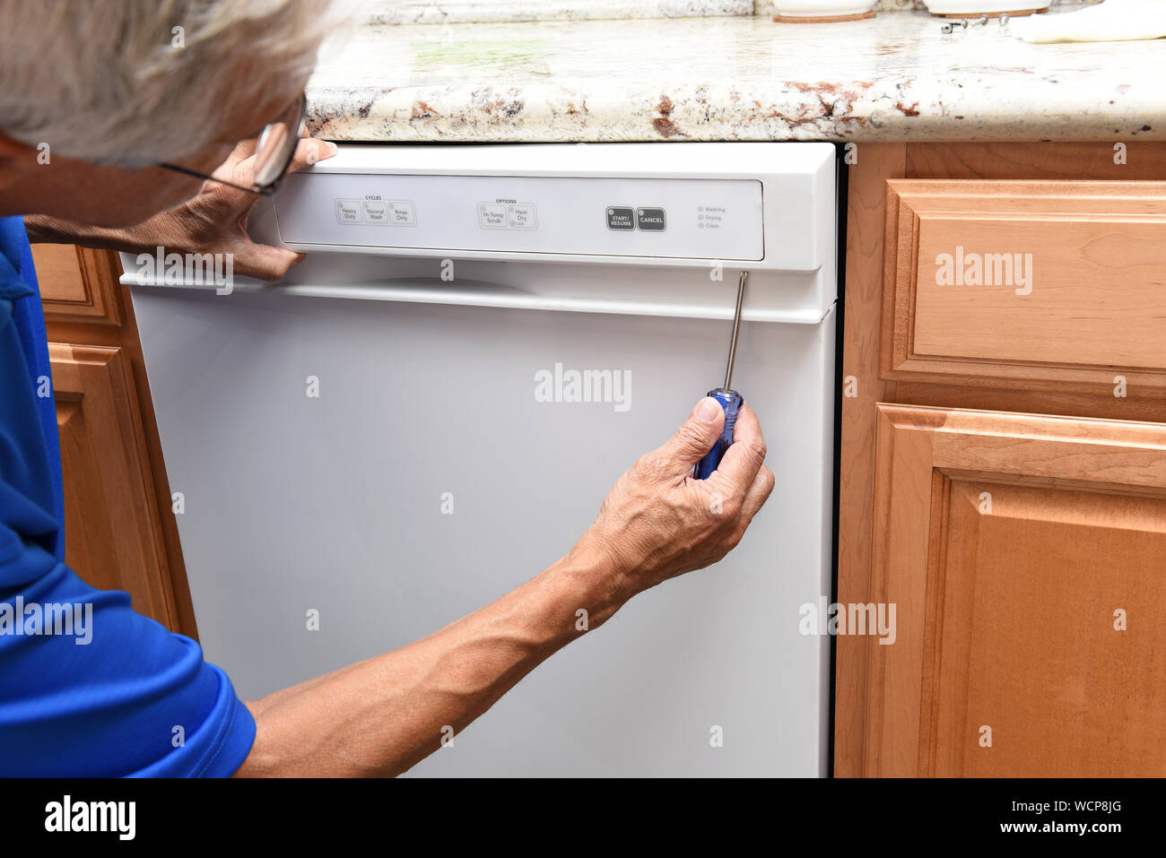 Closeup of a appliance repairman using a screwdriver to remove the control panel on a broken dishwasher. Stock Photo