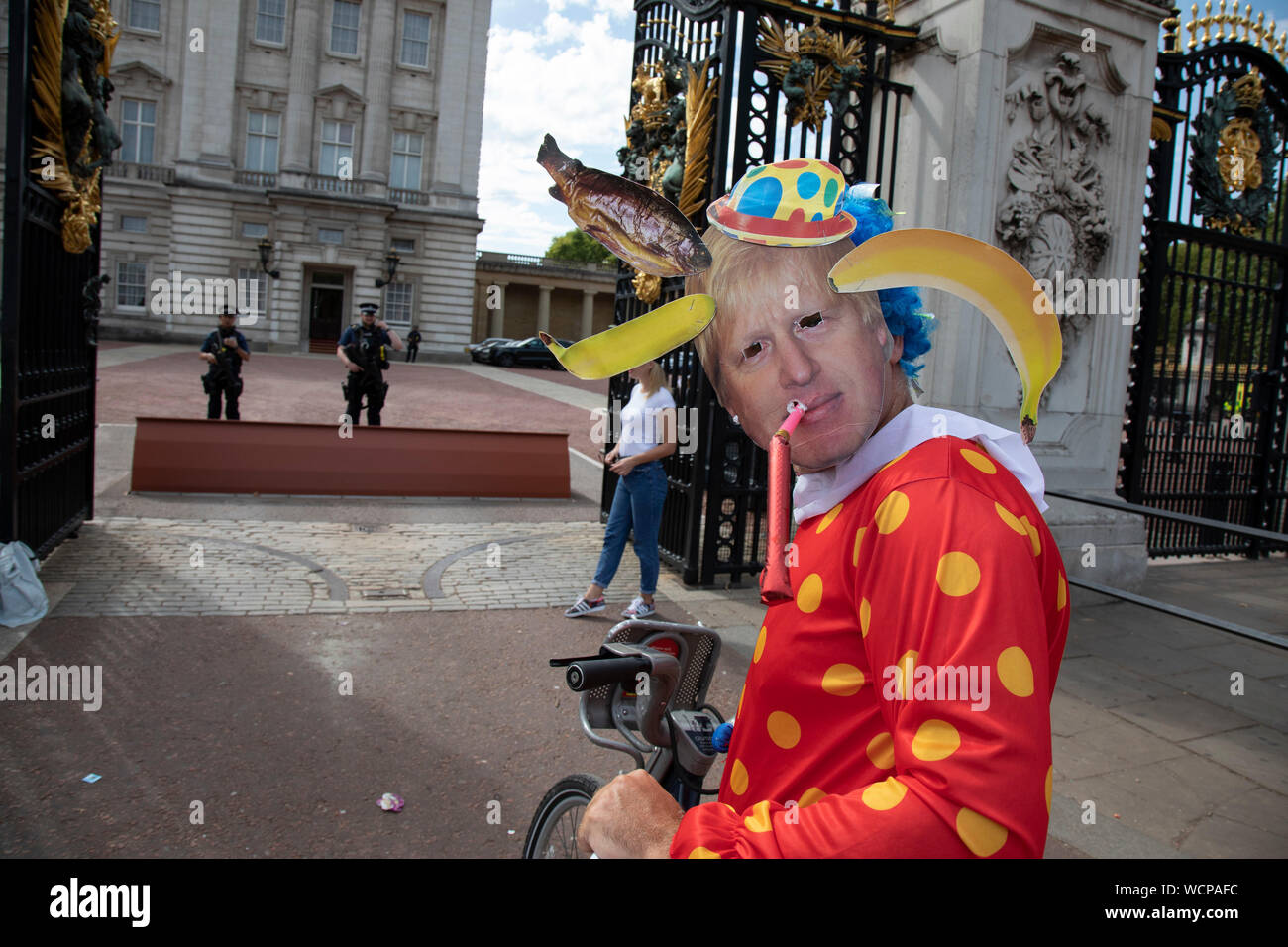Anti Brexit protester dressed up as a clown version of Prime Minister Boris Johnson hires a Boris bike in Westminster and cycles to the gates of Buckingham Palace as it is announced that Boris Johnson has had his request to suspend Parliament approved by the Queen on 28th August 2019 in London, England, United Kingdom. The announcement of a suspension of Parliament for approximately five weeks ahead of Brexit has enraged Remain supporters who suggest this is a sinister plan to stop the debate concerning a potential No Deal. Stock Photo
