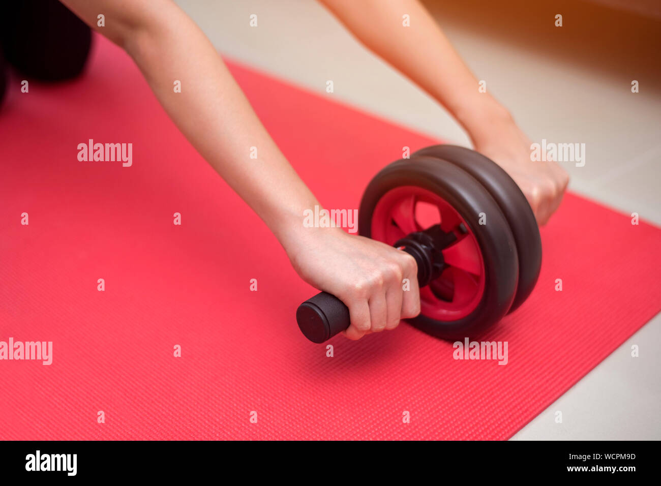 Cropped Hands Of Young Woman Holding Abdominal Toning Wheel On Exercise Mat At Home Stock Photo