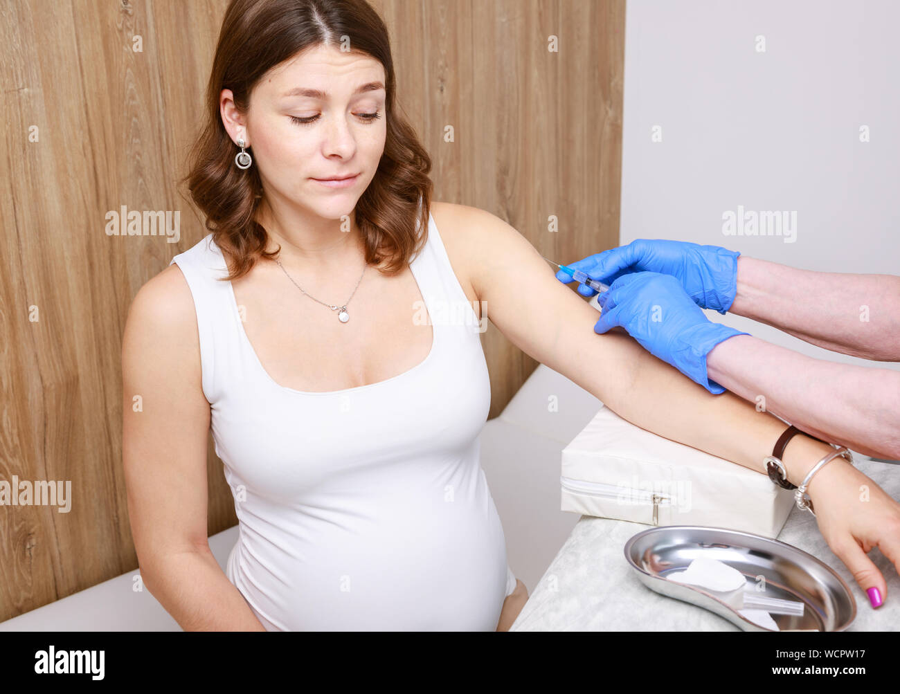 Medical assistant giving an intramuscular injection of a vaccine to arm of pregnant woman in a clinic - pregnancy vaccination concept Stock Photo