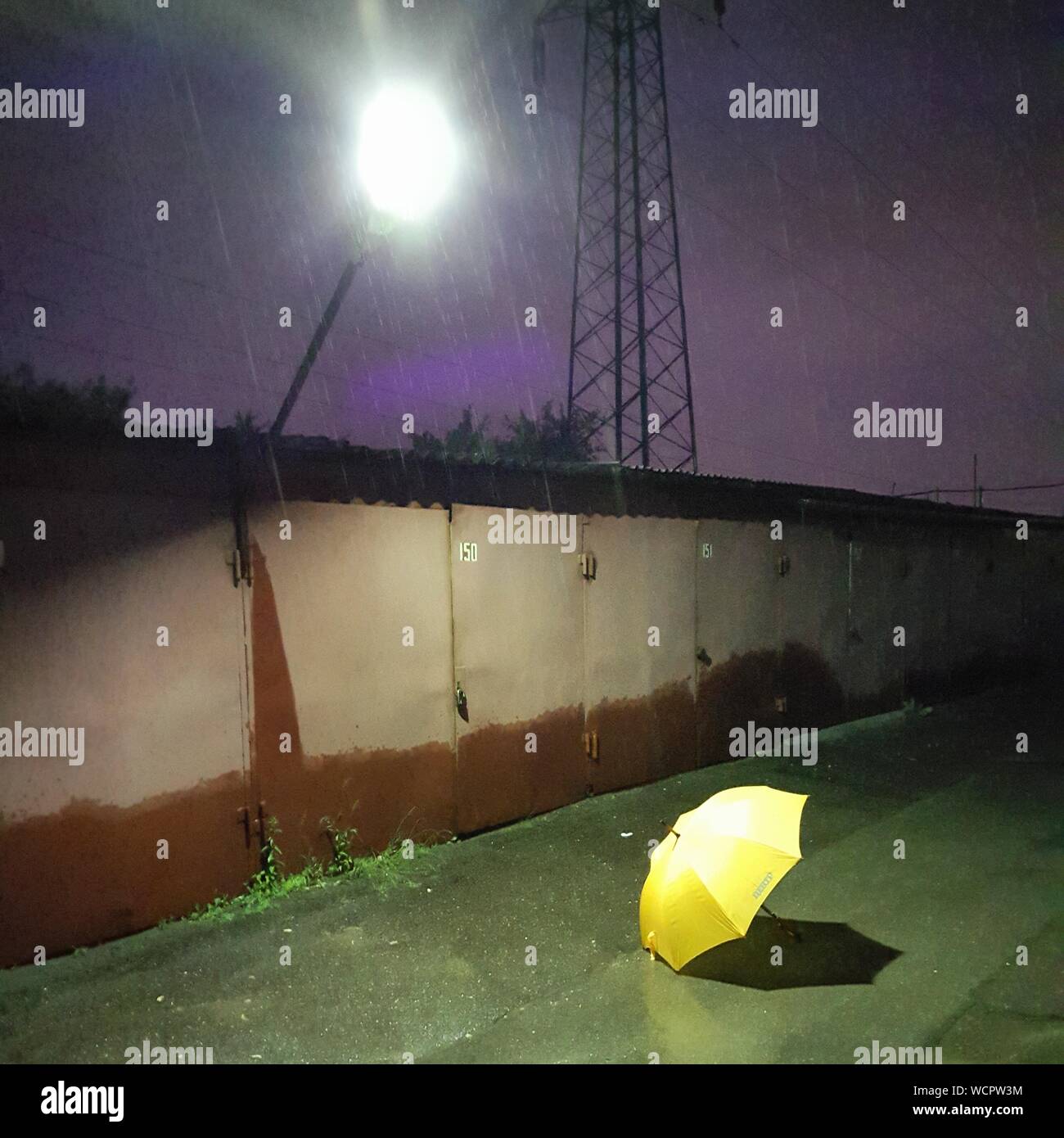 Umbrella On Footpath By Surrounding Wall At Rainy Night Stock Photo