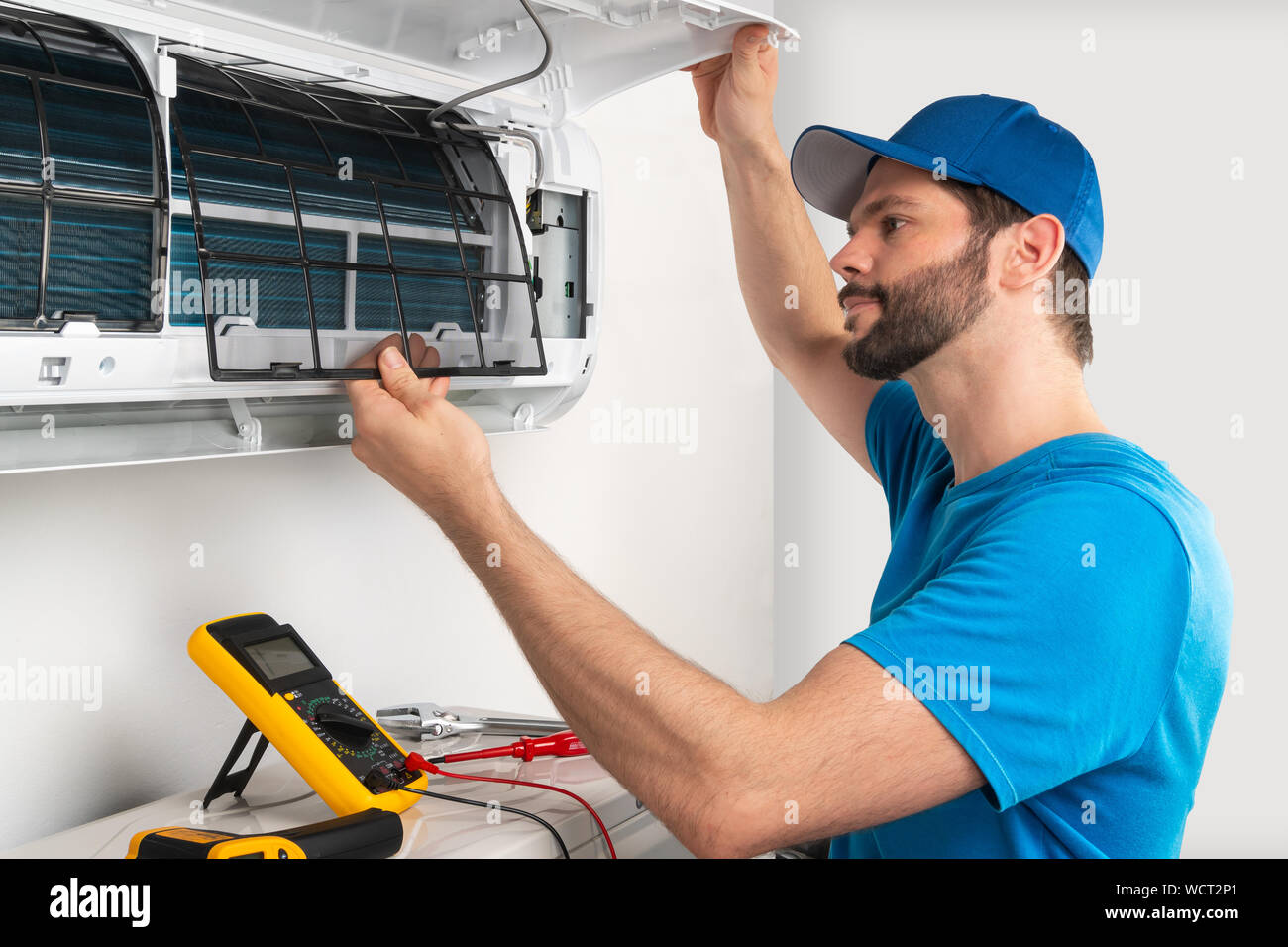 Installation service fix  repair maintenance of an air conditioner indoor unit, by cryogenist technican worker checking the air filter in blue shirt a Stock Photo