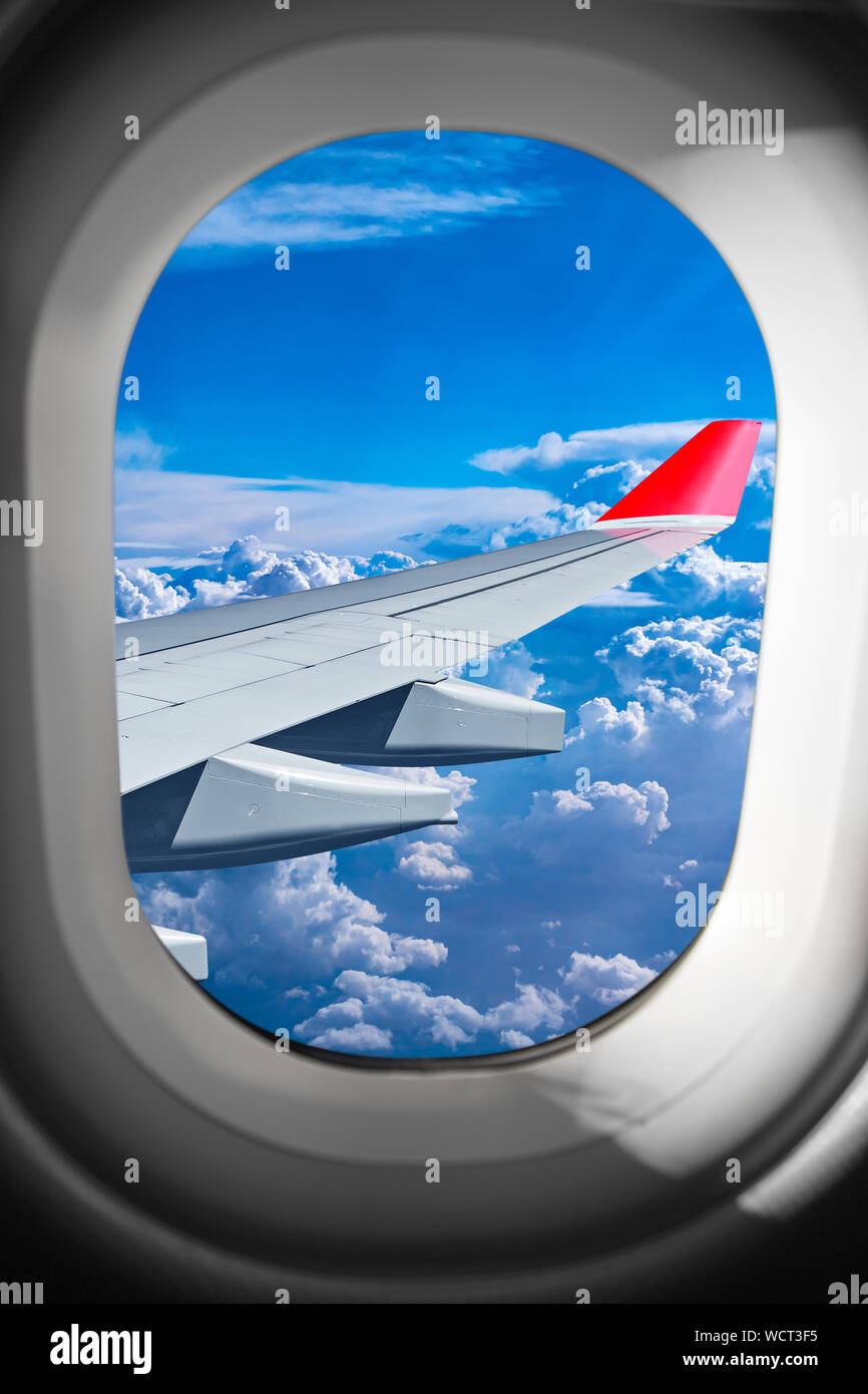 view through airplane window on plane flight wing in front of blue white cloud sky. transportation air travel fly concept Stock Photo
