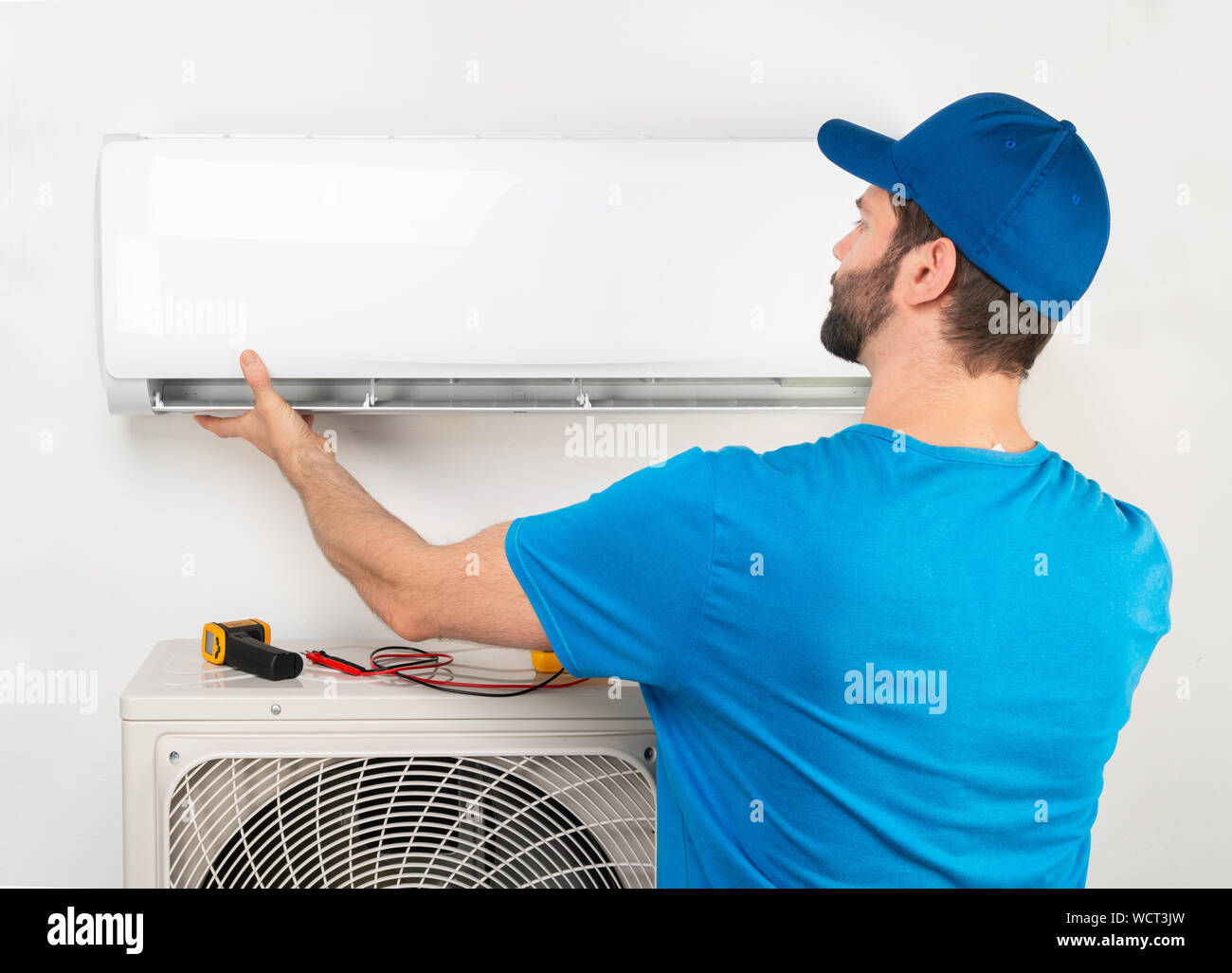 Installation service fix  repair maintenance of an air conditioner indoor unit, by cryogenist technican worker in blue shirt and baseball cap Stock Photo