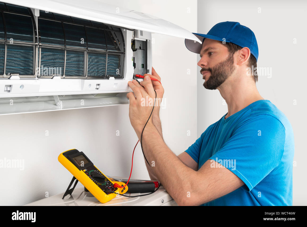 Installation service fix  repair maintenance of an air conditioner indoor unit, by cryogenist technican worker with multimeter checking electric blue Stock Photo