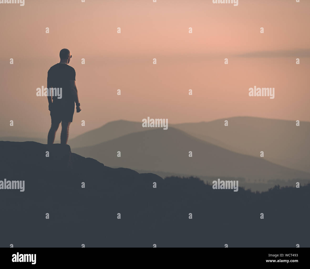 Young confident muscular male stood with a silhouette of mountains in the distance Stock Photo