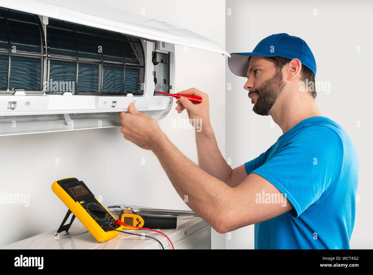 Installation service fix  repair maintenance of an air conditioner indoor unit by cryogenist technican worker with screwdriver  blue shirt and basebal Stock Photo