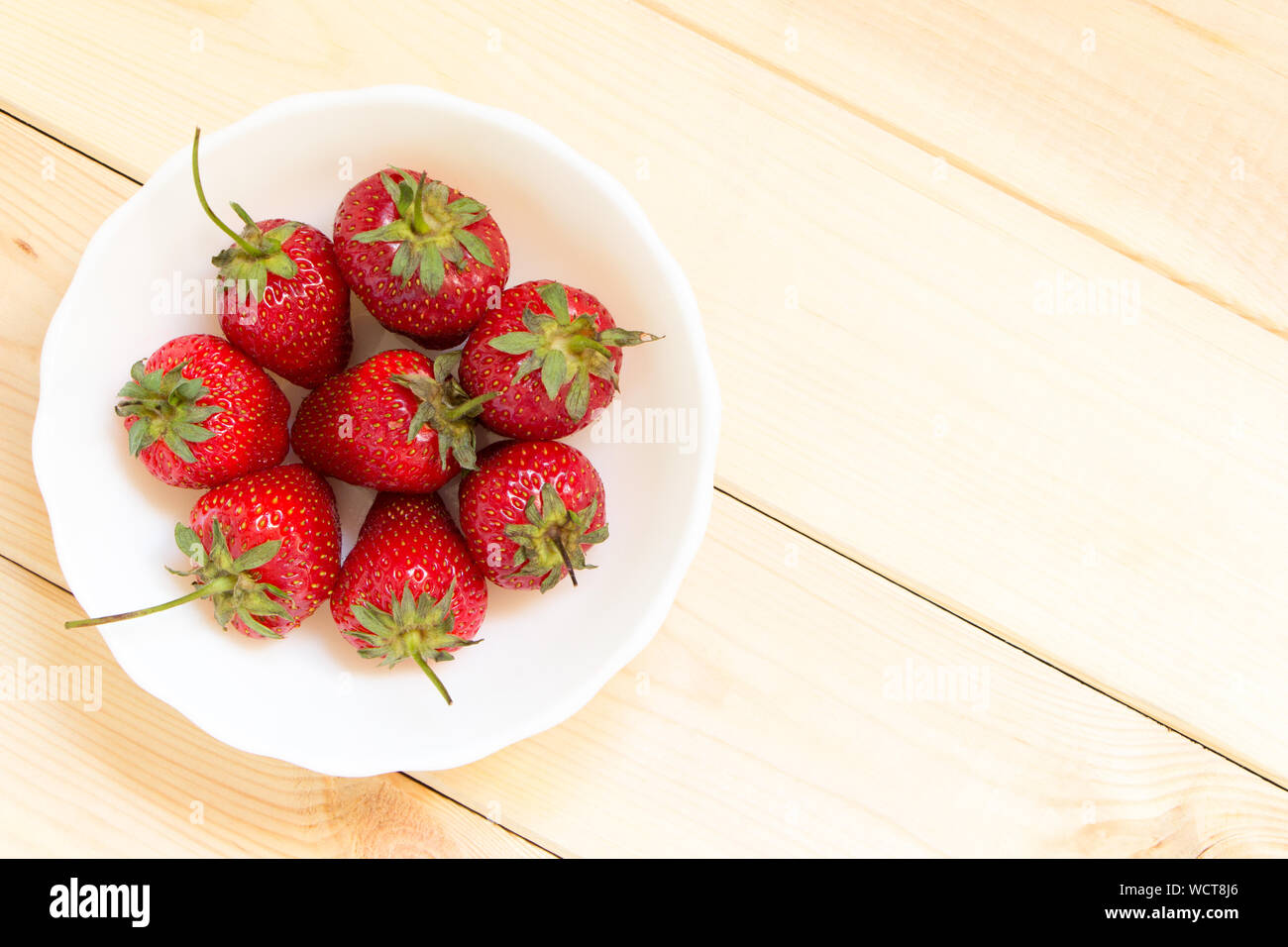Close-up summer harvest of red strawberries in white bowl on wooden table with copy space. Top angle view. Natural organic food concept. Background wi Stock Photo