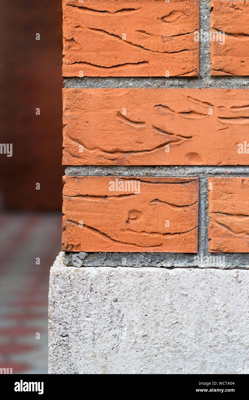 Outside corner of the house, lined with orange hardened brick. Weathered and dirty texture of wall. Close-up view. The concrete foundation is in the f Stock Photo