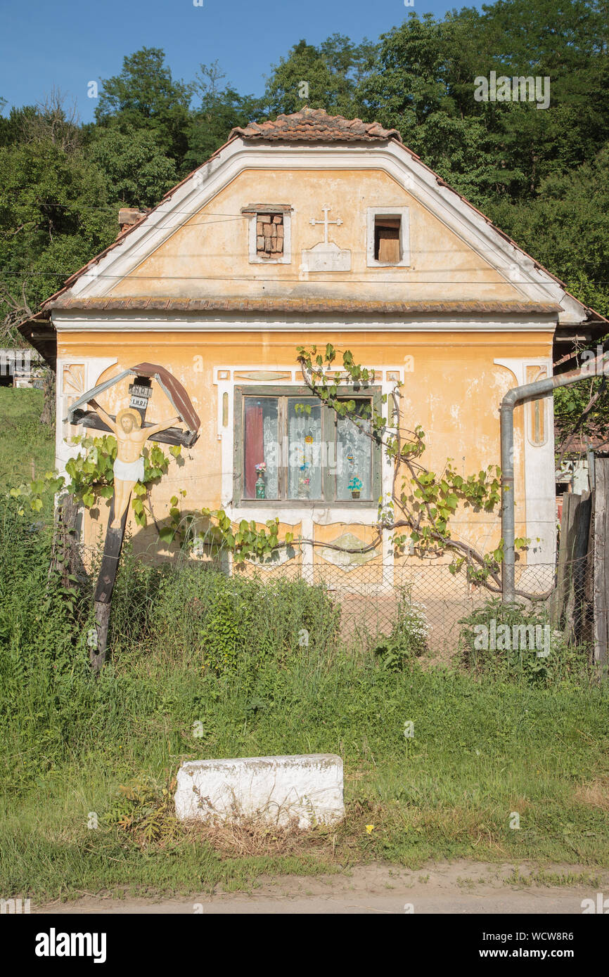 A painted crucifix in front of a decorated yellow ochre house in the village of Malancrav, Transylvania, Romania Stock Photo