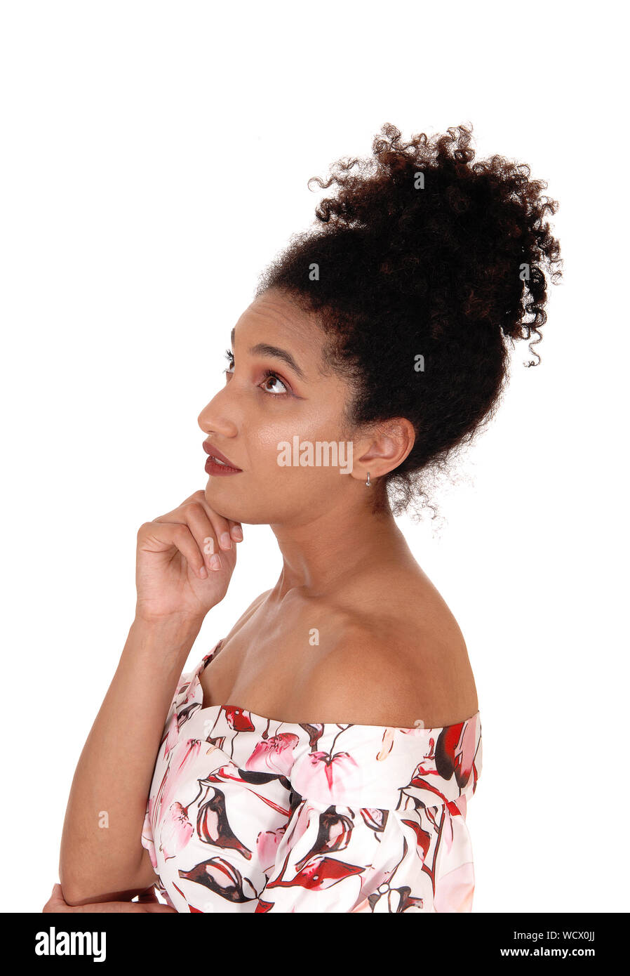 A close up image of a multi-racial woman standing in profile in a summer dress holding her hand on her chin with a slim figure and curly black hair, i Stock Photo