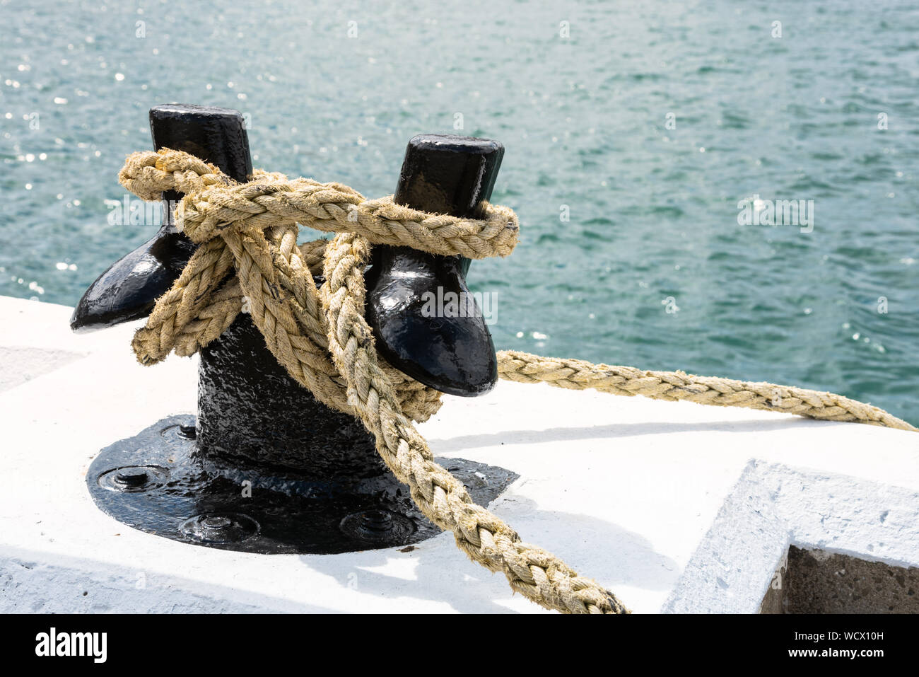 Close up of a mooring rope knotted to a black bollard Stock Photo