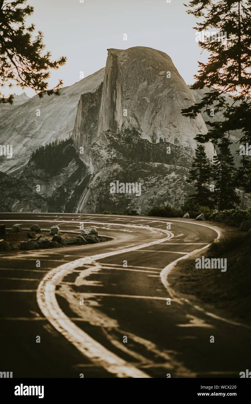 Vertical shot of a road near a mountain surrounded by trees Stock Photo ...