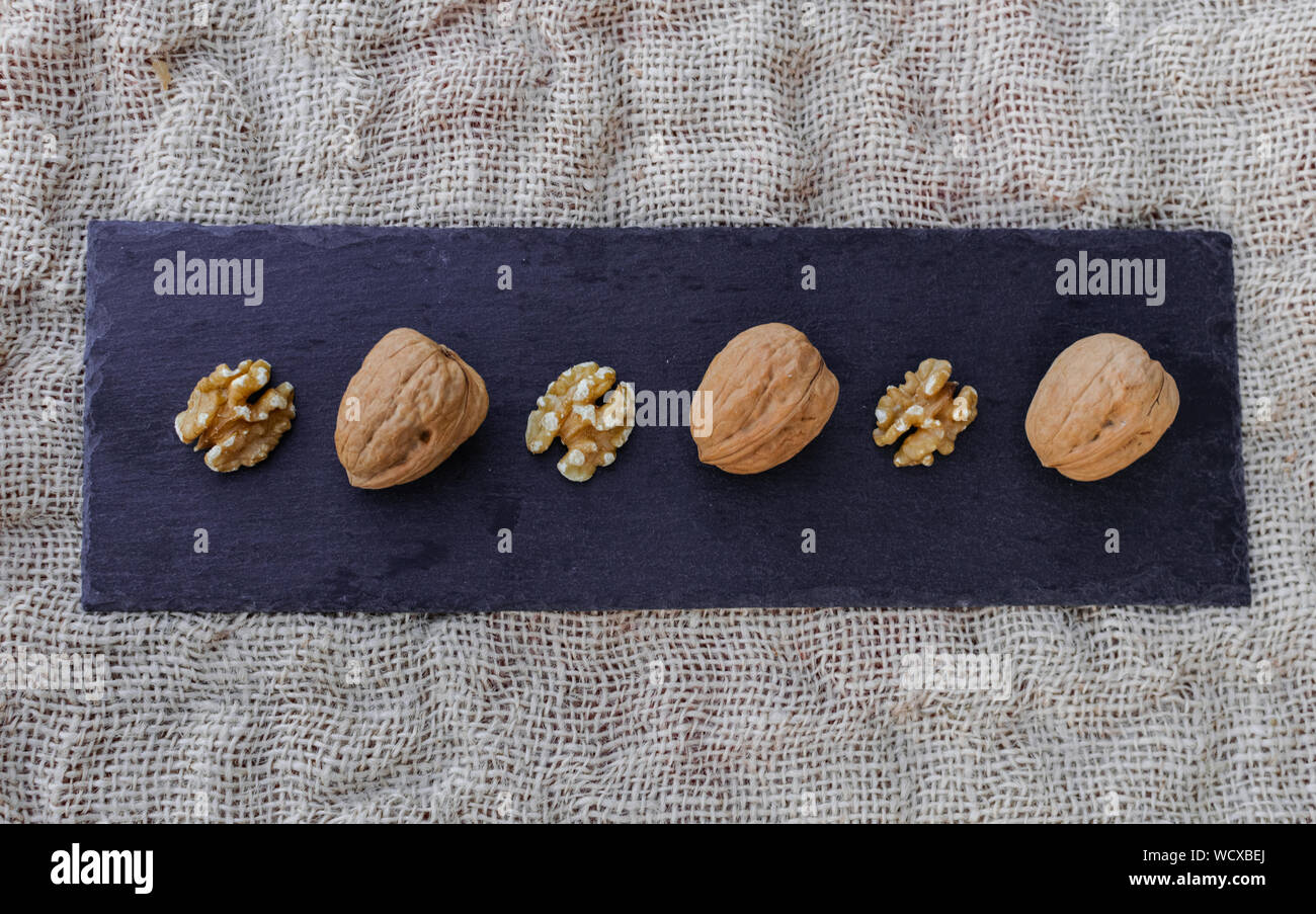 Walnuts, with and without shell, on black table surface, over sack texture Stock Photo