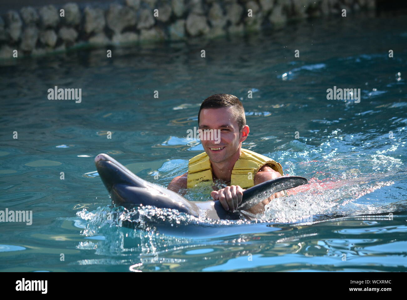 Smiling Young Man Holding Dolphin In Sea Stock Photo
