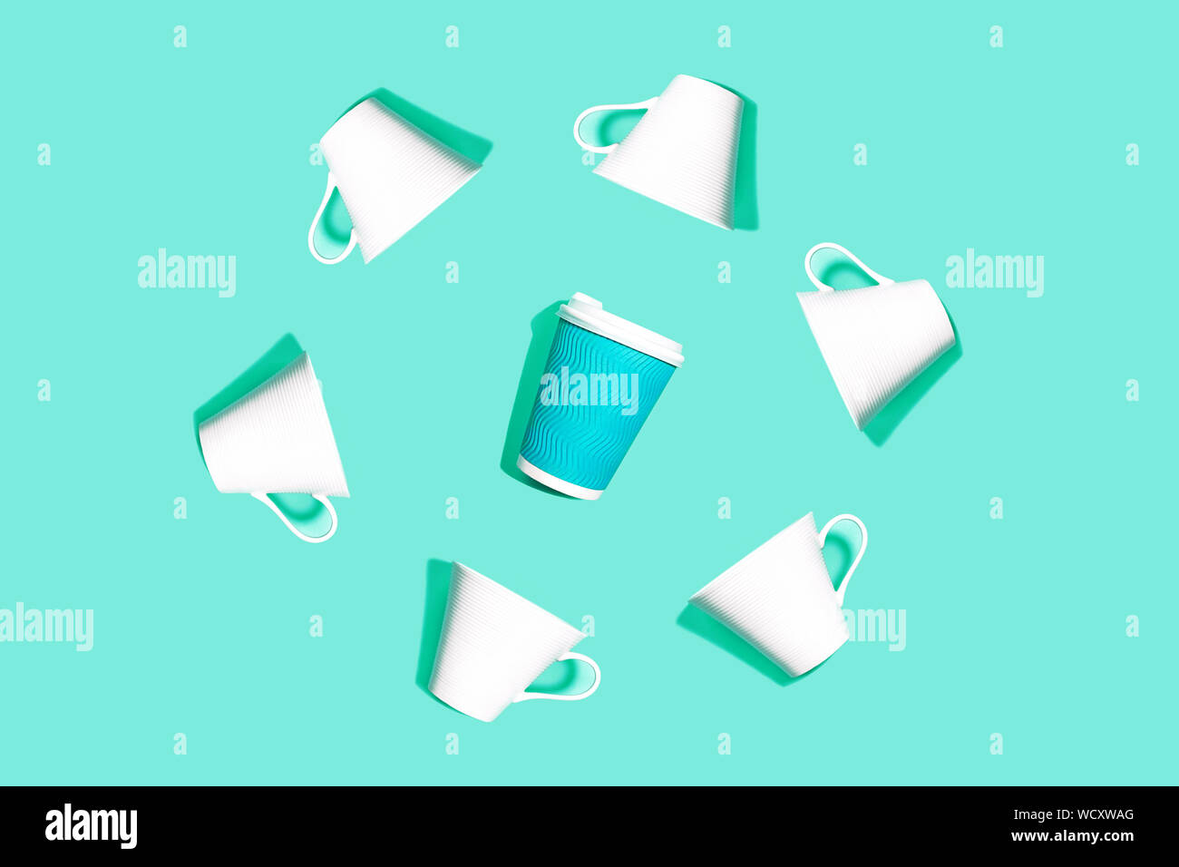 Coffee pattern is made from blue paper cup for coffee and white ceramic cups on bright mint background. Stock Photo
