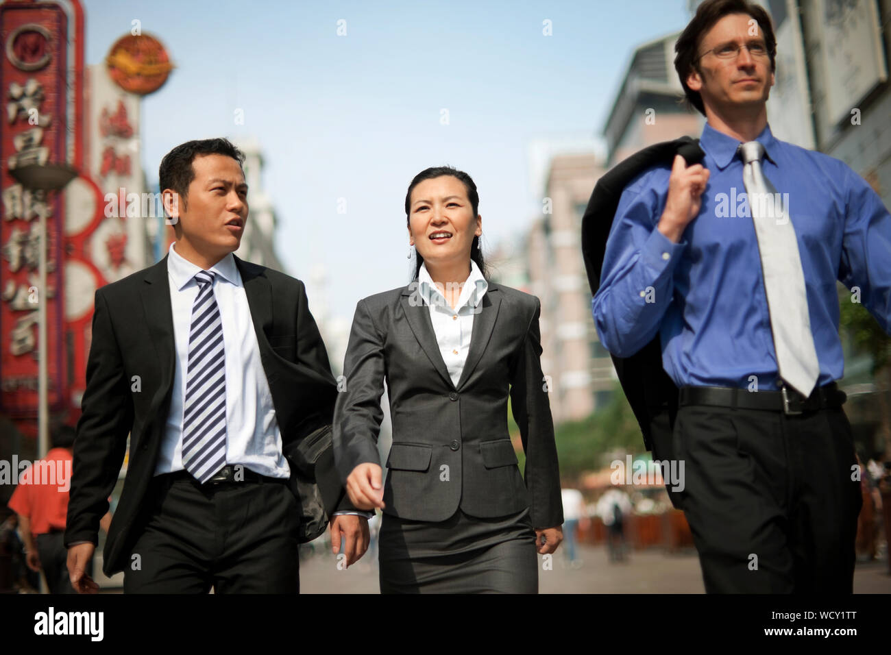 Three business colleagues walking down a busy street while talking. Stock Photo