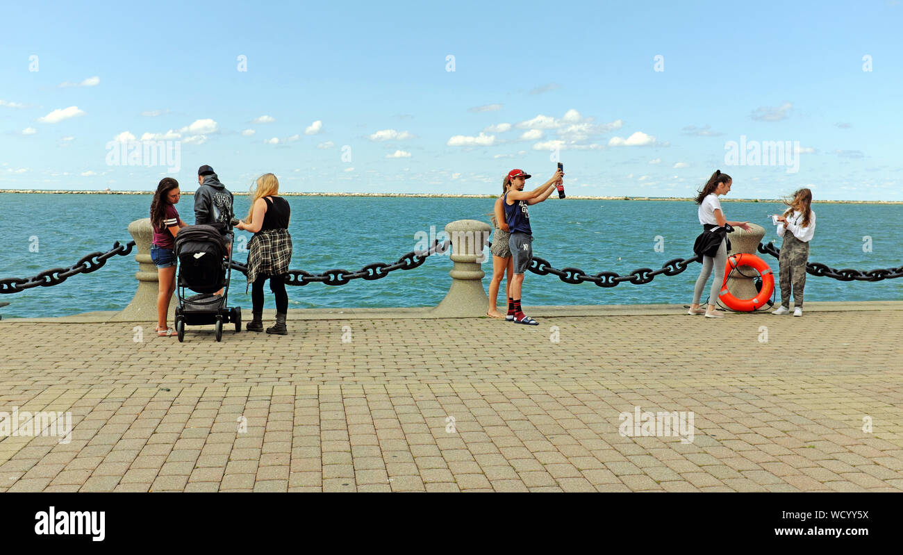 Visitors to Voinovich Park on the Northcoast Harbor in Cleveland, Ohio, USA stand next to Lake Erie during late summer warm weather. Stock Photo