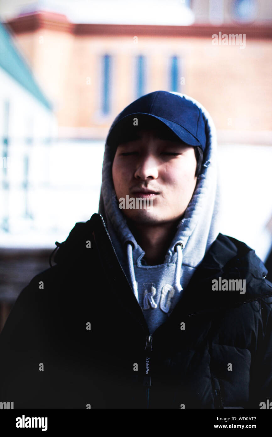 Young Man Wearing Hooded Jacket Sitting With Eyes Closed Stock Photo