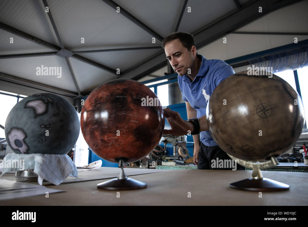 Athens, Greece. 27th Aug, 2019. Michael Koimtzis checks a handmade globe in his workshop near Athens, Greece, on Aug. 27, 2019. Globes of different sizes, lying on the floor, hung on shelves or on the ceiling, at different stages of production - either white, with their maps drying on strips of paper waiting for their assembly, or ready for delivery to the customer. This is the scene in 'Cosmic', the first Greek company that make globes in different sizes and colors. TO GO WITH 'Feature: Greek family business preserves Art of Handmade Globes' Credit: Lefteris Partsalis/Xinhua Stock Photo