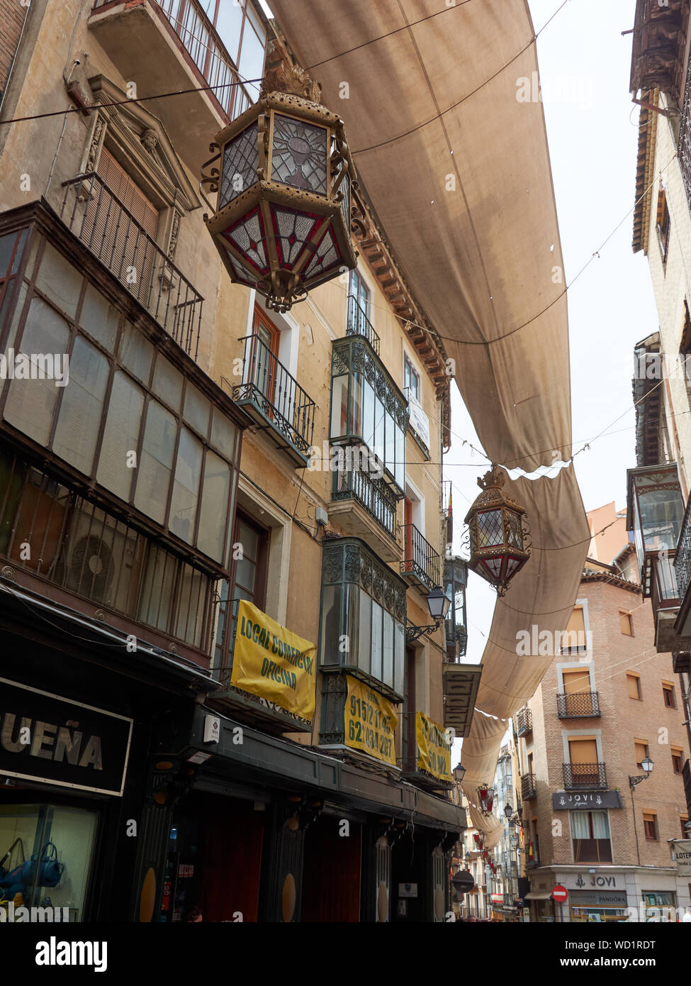 TOLEDO, SPAIN - APRIL 24, 2018: Stores, apartments and awning with lanterns in historical street of central Toledo. Stock Photo