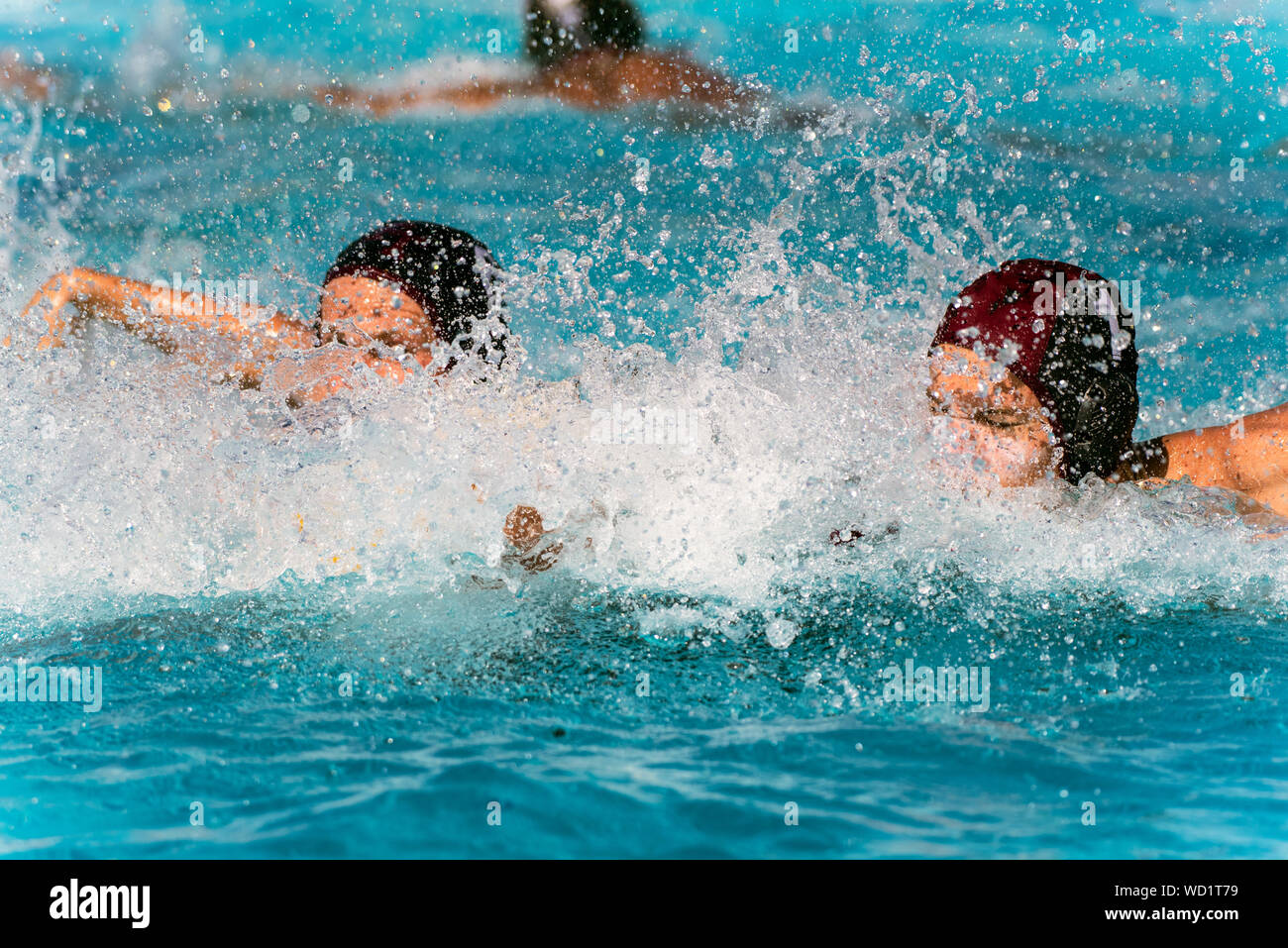 Water Polo team mates in black uniform covered by splashed water drops while racing to the defensive side of pool. Stock Photo