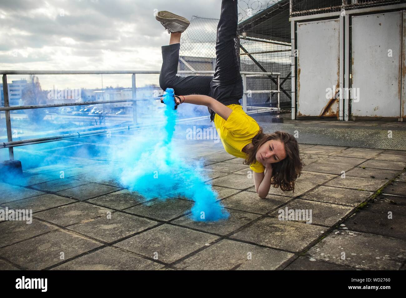 Young Woman With Smoke Bomb Doing Breakdancing On Roof Stock Photo