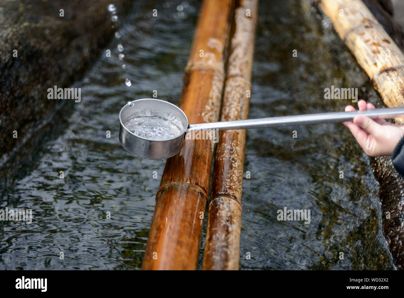 Cropped Hand Holding Ladle Over Bamboo And Water Stock Photo