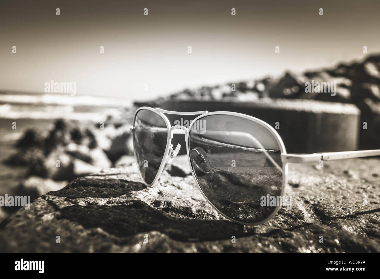 Close-up Of Sunglasses On Rock With Sea Reflection Against Sky Stock Photo