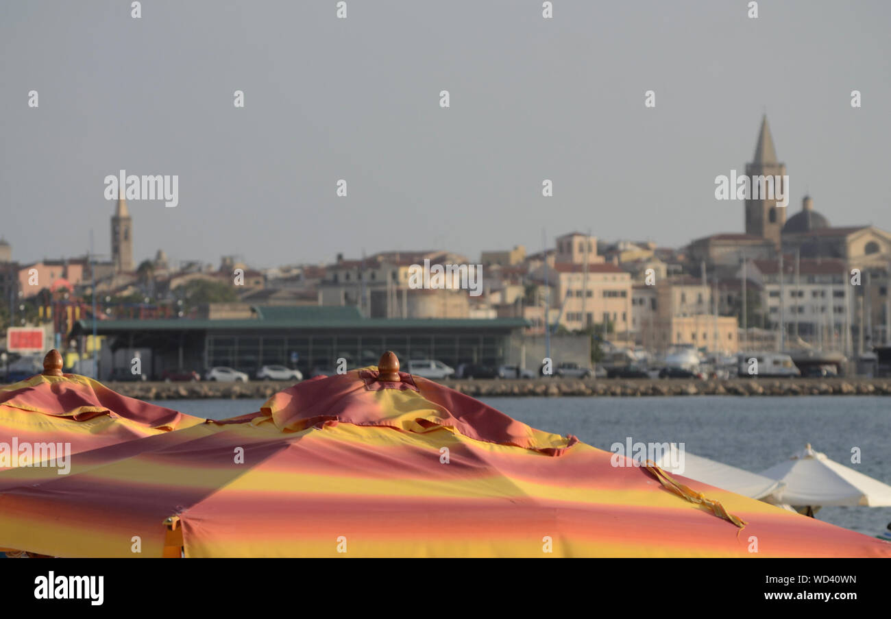 beach umbrella in the Lido di Alghero beach, on a summer day. The ancient city in the background Stock Photo