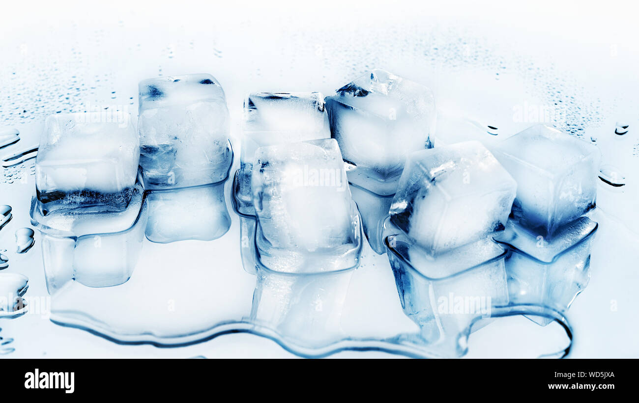 Ice cubes on white glass mirror background with reflection isolated close  up, a lot of blue transparent frozen crushed ice cubes, clear spilled water  drops, cold freshness drink ingredient, copy space Stock
