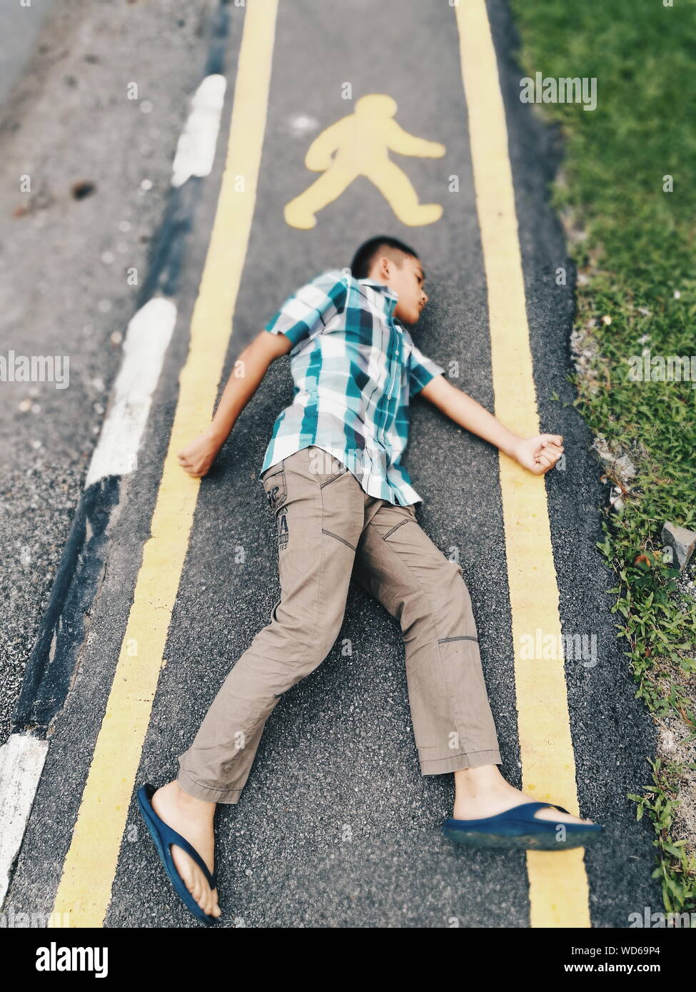 High Angle View Of Boy Imitating Pedestrian Sign On Road Stock Photo